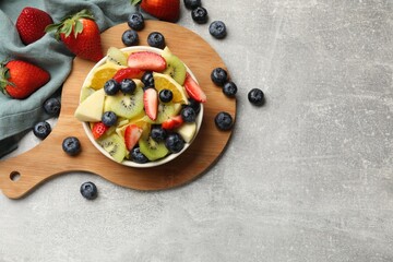 Tasty fruit salad in bowl and ingredients on gray textured table, flat lay. Space for text