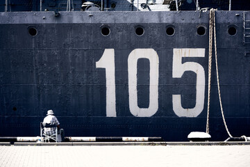 Old man fishing in front of a warship