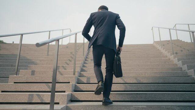 Follow shot of young businessman running up the stairsway rushing to work, salary man routine, working man holding business bag off to work, urban commuter being late to office, work punctuality 