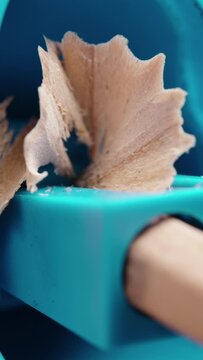 Vertical video. A wooden pencil is sharpened in a blue plastic sharpener, close-up.