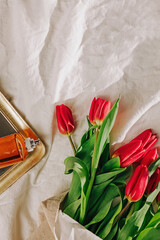 Red tulips and perfume bottle on the bed in natural sunlight, spring still life