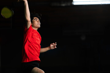 Badminton player in a jump smash with a racket in the air. Wearing a red shirt in a badminton...