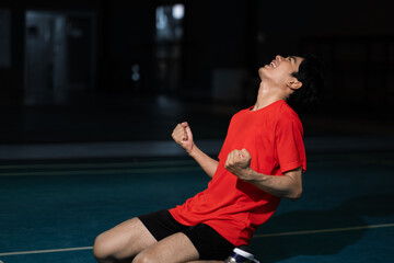 Badminton player celebrating victory on winning the game, and cheering with overwhelming excitement with fist thrusting. Male athlete wearing a red shirt, Sport activity and challenging concepts.