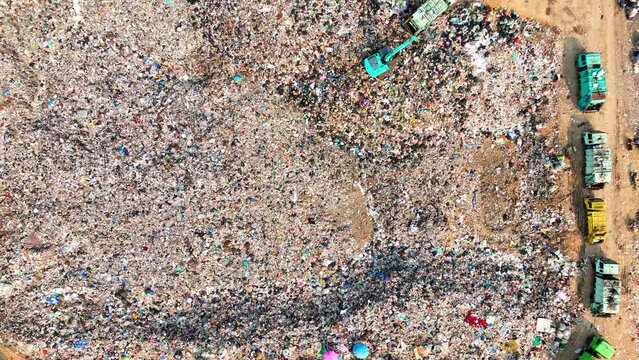 An aerial over the harsh truth: Landfill landscape marred by towering heaps of refuse, crisscrossed by dirt trails where solitary garbage trucks navigate, a poignant emblem of environmental hurdles.

