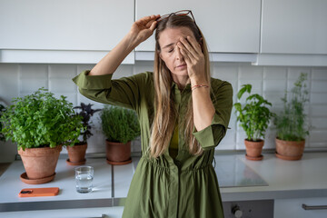 Sleepy woman suffering from chronic fatigue rubbing eyes on kitchen at home. Tired middle aged...