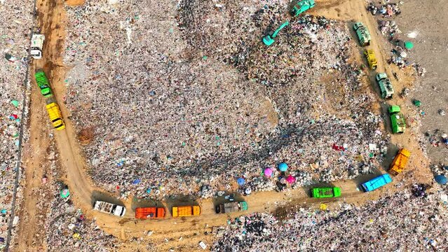 Surveying from on high, witness the expanse of a landfill. Mountains of garbage rise amidst crisscrossing trails, cloaked in plastic veils, as trucks trudge on, bearing the burden of society's excess.