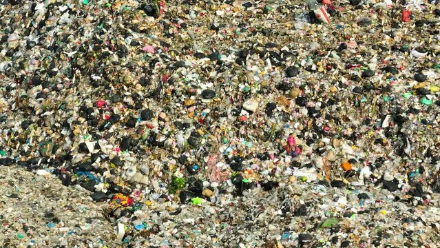 A dense mix of discarded items and debris, with notable patches of dirt and dark areas, perhaps liquid, showing the variety and complexity of waste in a landfill. Garbage background. 4K.
