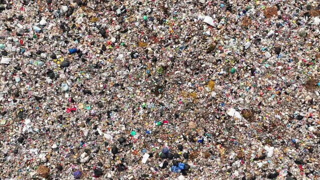 A drone surveys a sea of trash, a mosaic of hues and materials, sprawling across a vast landfill. Colors blend in chaos, revealing our society's discarded remnants in this waste disposal expanse.
