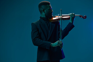 Elegant musician in black suit playing the violin on a vibrant blue background