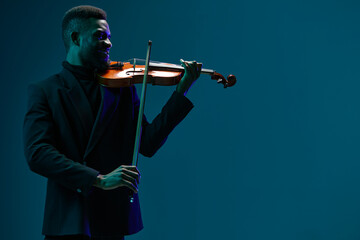 Elegant musician in black suit performing on violin against vibrant blue backdrop on stage