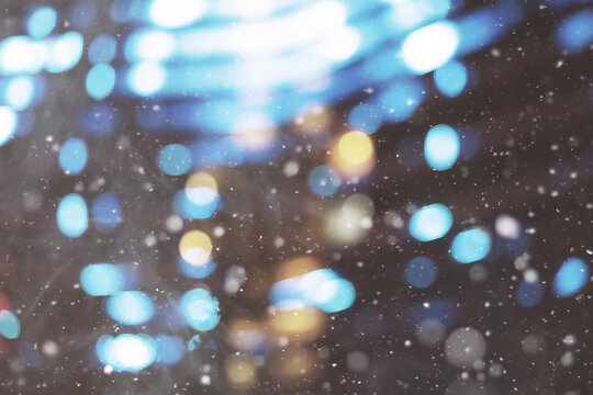 De focused/blur image of city at winter night. Snowflakes with blurred urban abstract traffic background.
