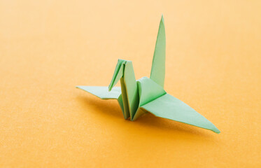 Green origami paper crane on yellow background