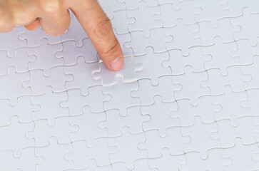 Hand putting the last piece of white jigsaw puzzle
