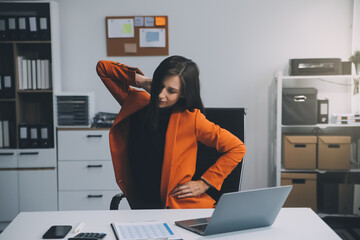 Asian woman working hard in the office having aches and pains in her torso and waist
