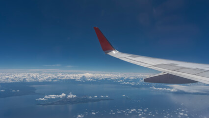 Fototapeta premium The blue ocean and tropical islands are visible from the plane. Clouds are reflected in the calm water. In the foreground is an airplane wing. Malaysia