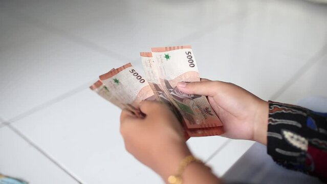 Woman counts many rupiah (IDR) Brown 5000 banknotes in hands with blurred background. Indonesian paper currency