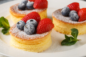 Japanese pancakes are fluffy, souffle-like pancakes that are airy perfection when topped with powdered sugar, blueberry and strawberry close-up on a plate on the table. Horizontal