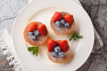 Japanese soft pancakes with berries sprinkled with powdered sugar close-up on a plate on the table. Horizontal top view from above