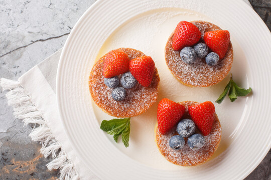 Japanese pancakes are fluffy, souffle-like pancakes that are airy perfection when topped with powdered sugar, blueberry and strawberry close-up on a plate on the table. Horizontal top view from above