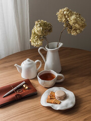 Aesthetic still life - a cup of tea, dessert, notebook, hydrangeas in a jug on a wooden table. Tea break
