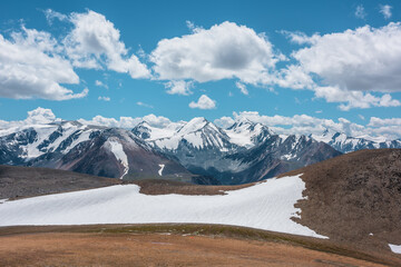 Aerial top view to stony pass and snow-white glacier on rocky hill in sunlight among high mountains in sunny day. Large colorful mountain range with snowy peaks in far away under clouds in blue sky. - 784252109
