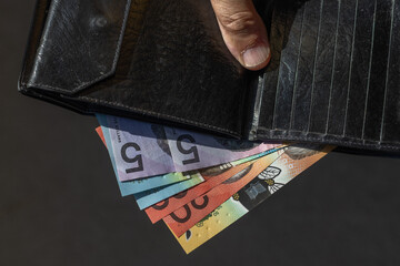 Close-up of Australian dollar banknotes displayed partially out of a black wallet in the sun, being...