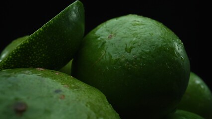 Slices of lime are meticulously arranged in a pile, set against a black background. Each lime slice is captured in stunning detail, its vibrant green hue and enticing texture. Close up. Comestible.