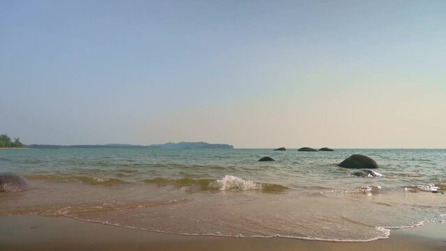 View from the beach with small waves crashing on the sand under afternoon sunlight during summer. Tranquil scene of west coast with blue sky in Thailand.