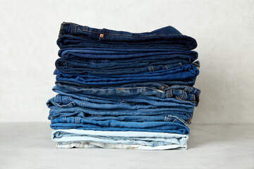 A stack of neatly folded jeans on a gray background. 