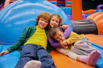 Cute little kids of different age playing on inflatable bounce house - obrazy, fototapety, plakaty