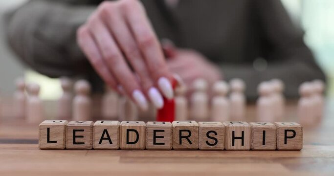 Word leadership and a hand placing red figurine and a group of identical wooden figurines