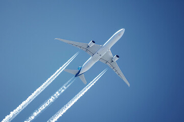 Photo of airplane at high altitude from below against blue sky. White marks from the engines are...