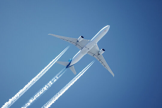 Photo of airplane at high altitude from below against blue sky. White marks from the engines are visible.