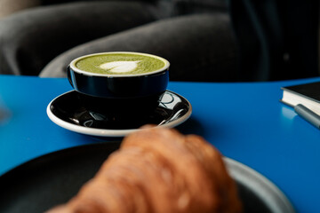 Cup with matcha latte and blurred croissant on the breakfast table