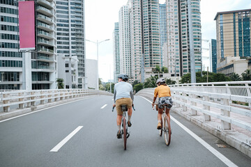 A couple is cycling in the city, crossing a bridge during summer time.