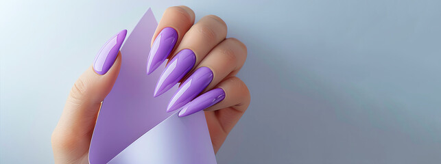 A hand holding a purple nail polish bottle with a purple paper in the background. Concept of elegance, sophistication, as the purple nail polish. an outstretched hand on paper, manicure details