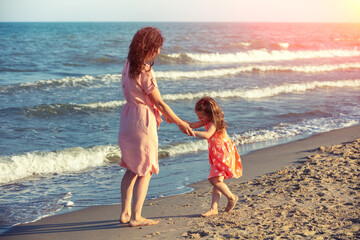 Young happy woman with little daughter dancing holding hands on the beach. Mother's Day concept