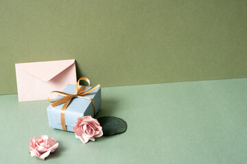 Blue gift box and envelope card with pink rose on green table. khaki wall background. birthday...