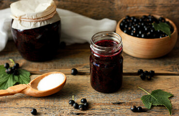 glass jar with black currant jam on a wooden background, around the ingredients for cooking a...