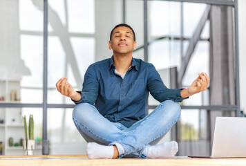 Calm African American young man sitting on the workplace in the office and meditation taking break avoiding stressful job