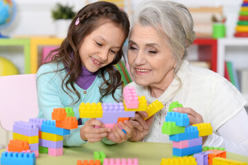 Cute girl and grandmother playing with colorful plastic blocks