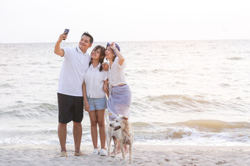 Happy Family with father mother and daughter selfie and looking smartphone and having fun on a tropical beach with dog. Family vacation holiday and travel concept