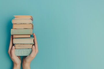 Woman's hands cradling a stack of books against a light blue backdrop, symbolizing education,...