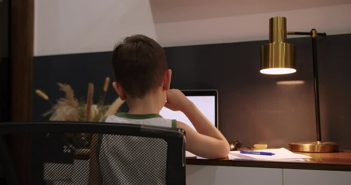 Back view child doing homework, cute kid a little boy studying at home. Kid cute little boy 8 old wearing studying from home. Teen school student learning in home making notes, doing homework. 4K