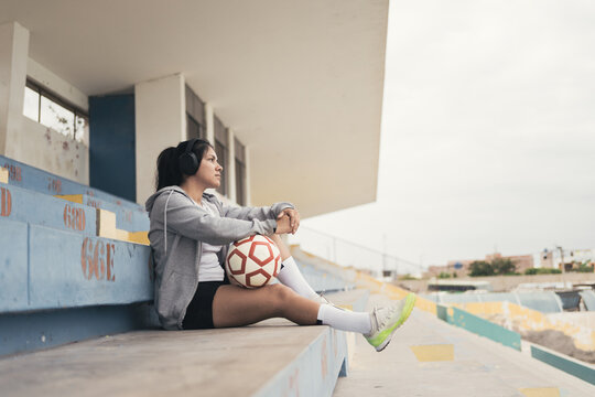 Young woman with soccer ball listening music through in headphones