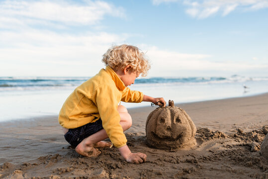 Curly haired child building a sand Jack-o-Lantern at beach