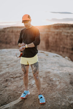 male runner with leg tattoos checks his watch at sunset, Utah desert