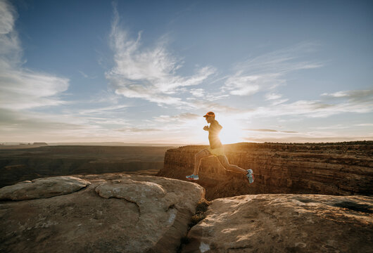 Male runner sprints along edge of desert cliff at sunset.