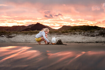 Happy child and dog playing at beach illuminated by pink sunset