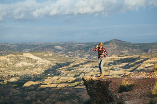 Woman in a plaid shirt and hat looking at the landscape from above.